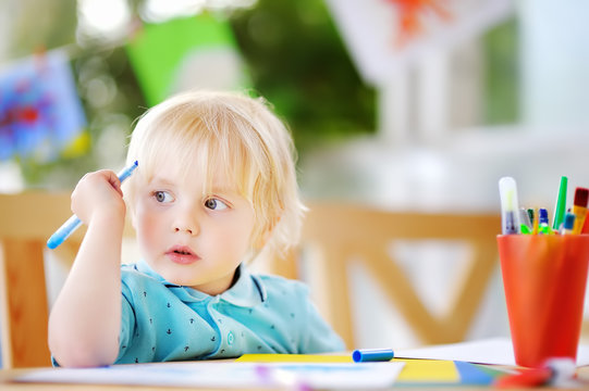Cute little boy drawing and painting with colorful markers at kindergarten
