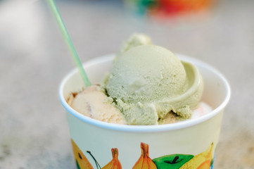 Several scoops of pistachio, stracciatella and vanilla flavored, original Italian ice cream in a typical paper, take away cup at a Gelateria in Germany