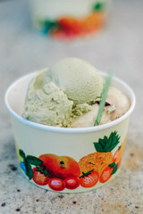 Several scoops of pistachio, stracciatella and vanilla flavored, original Italian ice cream in a typical paper, take away cup at a Gelateria in Germany