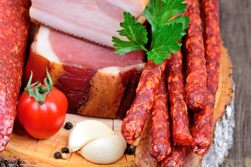 Bacon, prosciutto, dried sausages and salami with spices on a wood cutting board