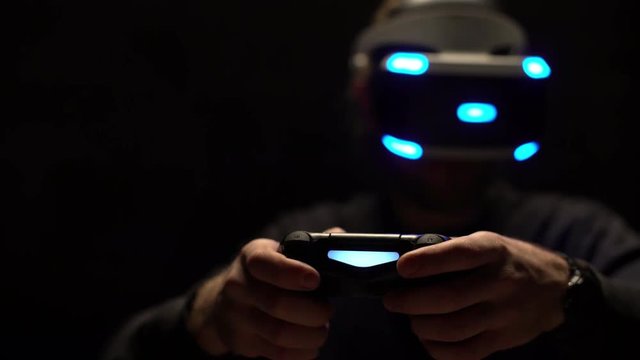 Portrait closeup of young man holding playing joystick enjoying video games and virtual reality experience, wearing digital glasses in dark room