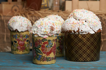 Kulichi, traditional Russian Easter cake with icing on rustic wooden table with straw on background
