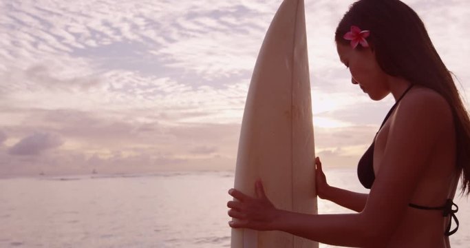 Surfing woman surfer silhouette with surfboard at sunset on tropical beach. Surfing girl looking at ocean. Female bikini woman by water standing with surfboard living healthy active lifestyle.