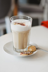 Latte macchiato, espresso with frothy milk, served in tall glass with cookies  on whtie table at coffee house