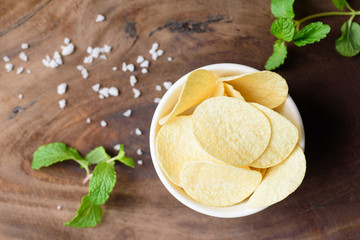 Potato chips in a bowl and salt on wooden background, top view of food