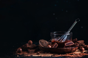 Melted chocolate glazing in a glass cup with a whisk. Dark chocolate and milk chocolate chunks with cinnamon and other spices on a black background.