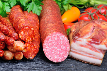 Sausages, salami and smoked bacon with vegetables on table