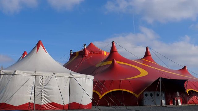 Two circus tents. White small and large red with closed entrance door on a sunny windy day