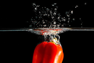 Red chilli pepperthrown into the water. Black background to see the freshness and bright colors of vegetables.