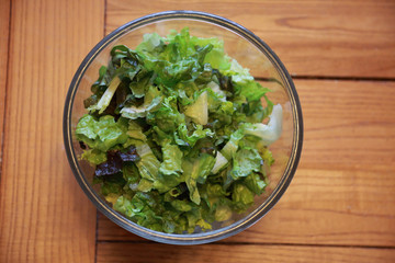 Lettuce salad in glass bowl on oak table viewed from above