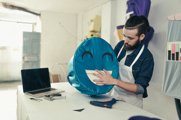 Young craftsman in the craft workshop customizing a carnival costume. Hipster working on his desk...