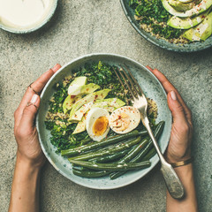 Healthy vegetarian breakfast bowls flat-lay. Quinoa, kale, green beans, avocado, egg and tahini dressing bowls over grey background, top view, square crop. Energy boosting, clean eating food concept