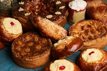 Homemade Russian Easter baked goods, kulichi, patties with cottage cheese, karavai and loaf cake with nuts on festive table background