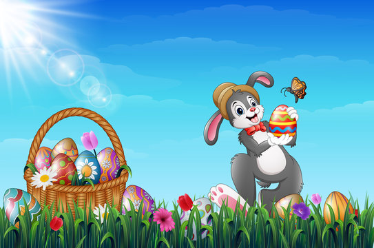 Easter bunny holding Easter eggs with a butterfly. Easter Wicker basket full of decorated Easter eggs in a grass field
