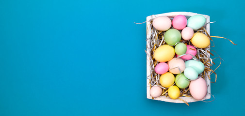 Multicolor eggs in a white tray. Creative Easter concept. Modern solid turquoise  background.