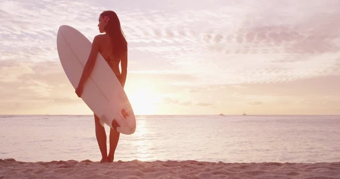 Fitness sport surfing on travel vacation - Surfer girl going surfing at beach sunrise. Female surfer woman looking at water with standing with surfboard having fun living healthy active lifestyle.