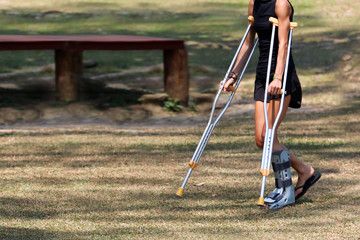 Accident tourist girl are walking by crutches in the garden.