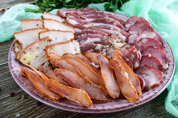 Big meat set. Homemade smoked pork-beef sausage, salted bacon, basturma chopped slices on a wooden board with spices and herbs.