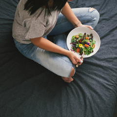 Young woman eating salad on bed home