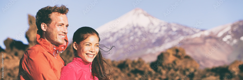 Wall mural couple hikers hiking looking at mountain landscape in outdoor nature. happy multiracial outdoors cou