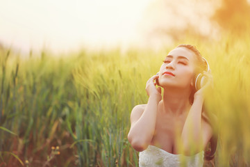 Beautiful young girl listening to music on headphones. The girl in the barley farm at sunset time.