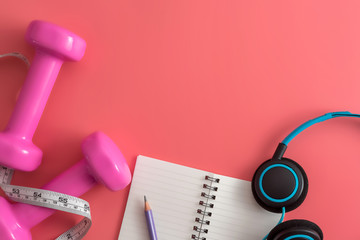 Styled stock photography of fitness equipment dumbbells notepad pencil and earphone on pink background. Flat lay.