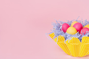 Easter painted eggs in fun yellow basket on soft pink background, copy space, closeup.