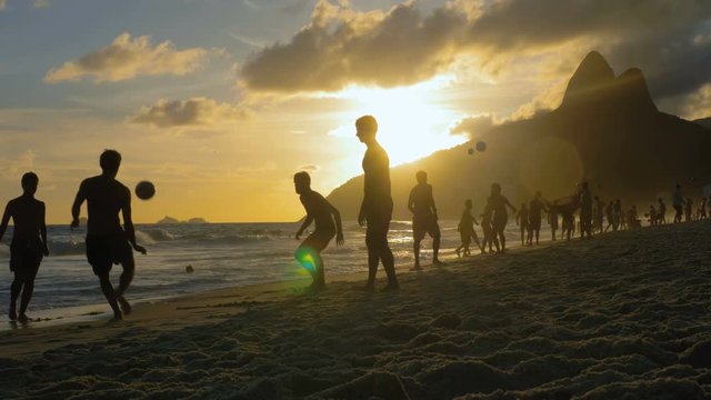 Playing beach football at sunset on Ipanema Beach, Rio de Janeiro. People silhouettes. Slow motion