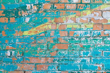 Old colorful (turquoise and yellow) paint with cracks on red brick wall as background, texture