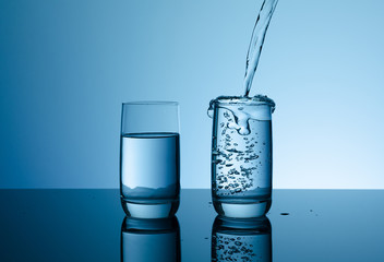 Creative splashing water in the glass on blue background.