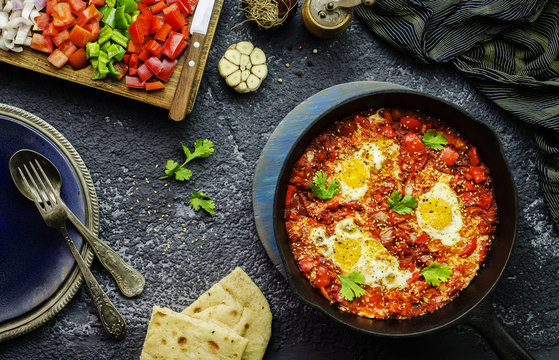 Middle Eastern traditional food; Shakshuka skillet served with pita bread and placed with fresh chopped vegetables. Top view with close-up