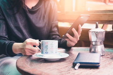The abstract image of the woman using a smartphone and hold a coffee cup in the vintage coffee shop. the concept of relaxing, coffee shop, jobs, freelance, technology and internet of things.