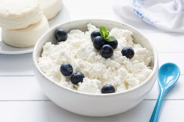 Cottage cheese, farmers cheese or tvorog in white bowl on white wooden table, closeup view