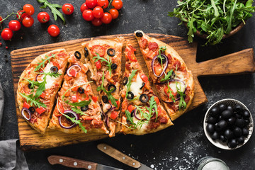 Flatbread pizza garnished with fresh arugula on wooden pizza board, top view. Dark stone background - 196977387