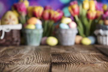 Easter background. Rustic wooden table. Tulips and spring flowers. Easter eggs. Colorful bokeh. Place for typography. 