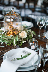 Guest card on a plate with wedding decorations in rustic style on a wooden table. Plate, napkin, candles, cloves and garlands.