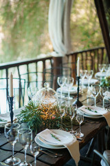 Guest card on a plate with wedding decorations in a rustic style in a gazebo near the water. Plate, napkin, candles, cloves and garlands.