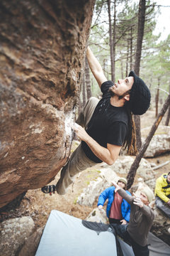 Rock climber with dreadlocks climbing overhanging boulder