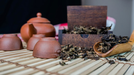 dried tea leaf in small wood box with wooden teaspoon tea pot and cup on bamboo mat