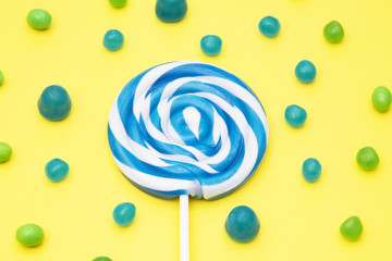colorful round lollipop and assortment of candies on yellow background