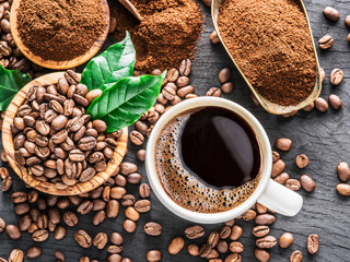 Roasted coffee beans, ground coffee and cup of coffee on wooden table. - obrazy, fototapety, plakaty