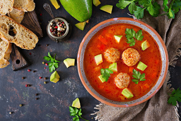 Spicy tomato soup with meatballs and vegetables. Served with avocado and parsley. Healthy...