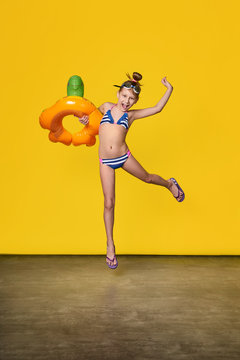 Beach Vacation concept.Funny girl teenager in bathing suit jumping up fun.Fashion child in movement smiles,emotion joy,happy.Full length, yellow background.Advertising rest, summertime, travel.