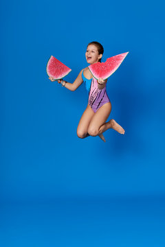 Beach Summer Vacation concept.Young girl jumping up fun on bright blue background as water sea.Cheerful child holding piece of watermelon.Energy caucasian teenage dressed in swimsuit for swimming.