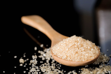 Brown sugar in wood spoon on black background.Components of The food is sweet delicious.