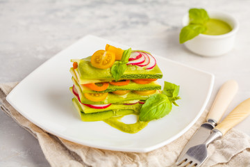 Raw vegan zucchini lasagna with vegetables and pesto sauce, light background. Vegetarian raw diet concept.