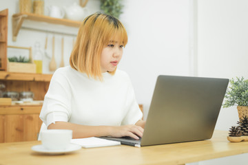 Beautiful young smiling Asian woman working on laptop while at home in office work space. Businesswoman working from home via portable computer writing on keyboard. Enjoying time at home.