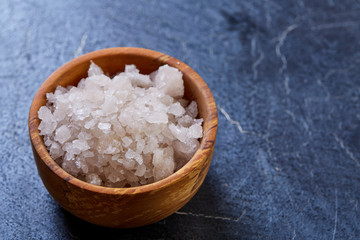 Large white sea salt in a natural wooden bowl on white background, top view, close-up, selective focus