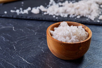Large white sea salt in a natural wooden bowl on white background, top view, close-up, selective focus