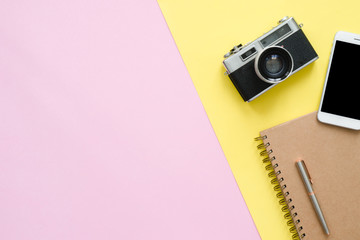 Flat lay design of travel summer concept - Top view of brown notebook, pencil, tablet and camera on pink and yellow pastel color screen with a copy space. travel summer on pastel color background.